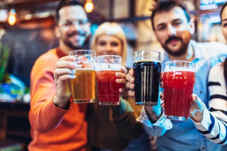 Téléchargez les photos : Souriant jeunes amis boire de la bière artisanale dans le pub - en image libre de droit