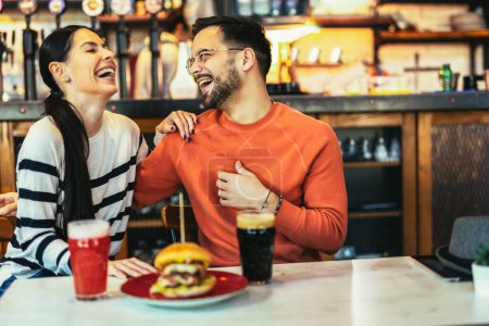 Téléchargez les photos : Jeune couple amoureux passer du temps libre ensemble au restaurant, manger des hamburgers et boire de la bière - en image libre de droit