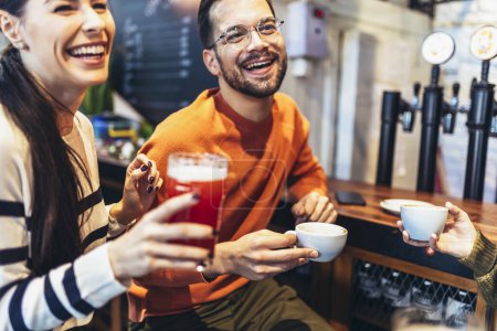 Téléchargez les photos : Souriant jeunes amis boire de la bière artisanale et du café dans le pub - en image libre de droit