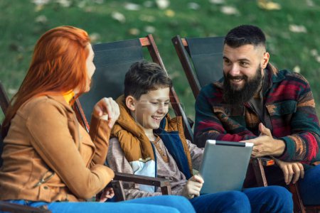 Foto de Familia joven disfrutando del tiempo en una cafetería al aire libre usando tableta digital. - Imagen libre de derechos