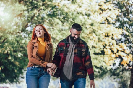 Téléchargez les photos : Jeune couple heureux se regardant tout en se tenant la main et en marchant dans le parc. - en image libre de droit