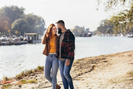Téléchargez les photos : Heureux jeune couple amoureux se tenant la main et marchant sur la côte près de la rivière. - en image libre de droit