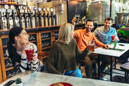 Foto de Sonrientes jóvenes amigos bebiendo cerveza artesanal en el pub - Imagen libre de derechos