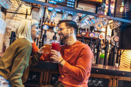 Photo for Smiling young couple at the bar with different varieties of craft beers toasting - Royalty Free Image