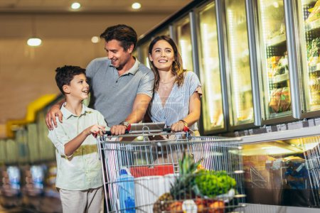 Happy family with child and shopping cart buying food at grocery store or supermarket