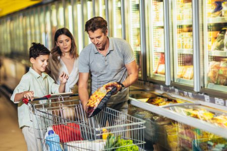 Happy family with child and shopping cart buying food at grocery store or supermarket