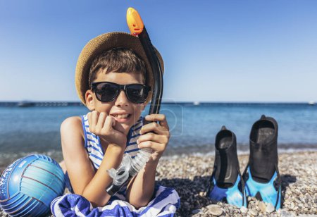 Téléchargez les photos : Happy boy has water polo ball and scuba gear on the beach. Looking at camera. Concept of travel, tourism, family. - en image libre de droit