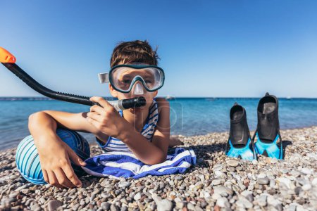 Téléchargez les photos : Happy boy a boule de water-polo et équipement de plongée sur la plage. Je regarde la caméra. Concept de voyage, tourisme, famille. - en image libre de droit