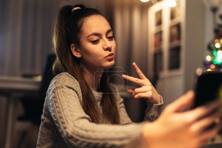 Photo for Smiling teenage girl taking selfie at home using smartphone - Royalty Free Image
