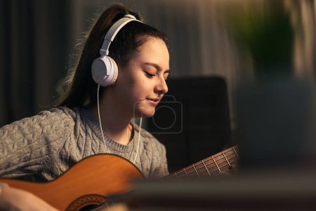 Foto de Caucasian teenage girl sits on floor and plays an acoustic guitar - Imagen libre de derechos
