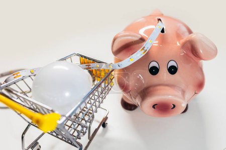 Téléchargez les photos : Piggy bank with light bulb and led light strip. Saving energy. - en image libre de droit