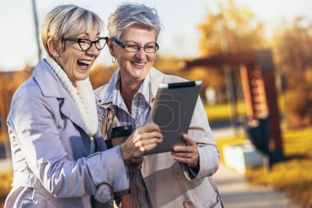 Téléchargez les photos : Deux amies âgées utilisant une tablette numérique dans le parc - en image libre de droit