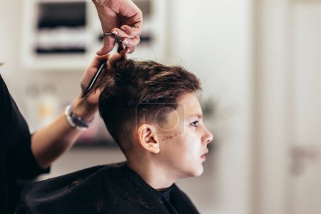 Foto de Cute young boy getting a haircut by hairdresser - Imagen libre de derechos