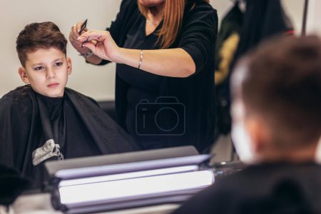 Téléchargez les photos : Cute young boy getting a haircut by hairdresser - en image libre de droit
