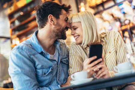Foto de Joven pareja feliz usando teléfono inteligente en la cafetería - Imagen libre de derechos