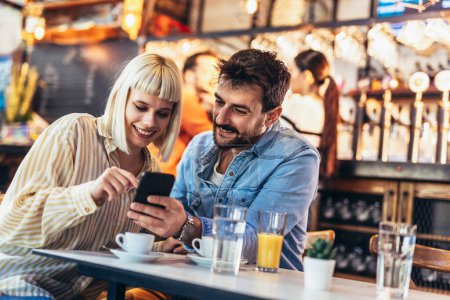 Foto de Joven pareja feliz usando teléfono inteligente en la cafetería - Imagen libre de derechos
