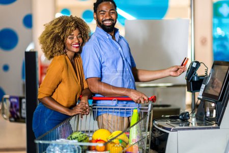 Téléchargez les photos : African American Couple with bank card buying food at grocery store or supermarket self-checkout - en image libre de droit