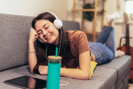 Téléchargez les photos : Young teen girl using digital tablet computer listening music at home - en image libre de droit