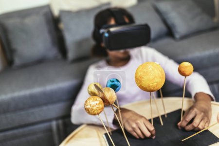 Téléchargez les photos : Happy african american school girl making a solar system for a school science project at home using VR glasses to immerse herself in metaverse - en image libre de droit