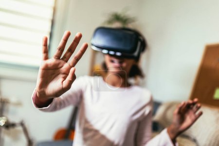Photo for African American girl using virtual reality glasses in her room. Black girl enjoys VR technology to watch 3D movies or immerse herself in metaverse - Royalty Free Image