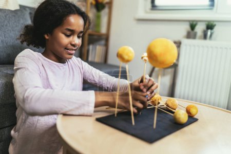 Photo for Happy african american school girl making a solar system for a school science project at home - Royalty Free Image