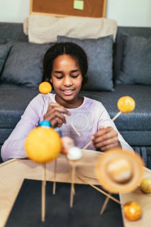 Téléchargez les photos : Happy african american school girl making a solar system for a school science project at home - en image libre de droit