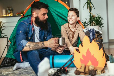 Photo for Dad with his son camp inside their home. They have pitched a tent and have a fake campfire. - Royalty Free Image