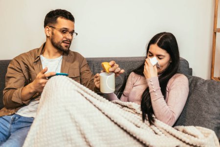 Photo for Sick young couple drinking hot tea and blowing nose at home - health, flu and people concept - Royalty Free Image
