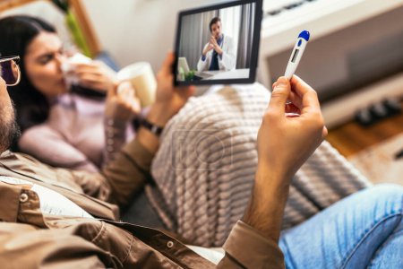 Téléchargez les photos : Jeune couple malade ayant téléconsultation médicale à l'aide d'une tablette numérique à la maison. - en image libre de droit