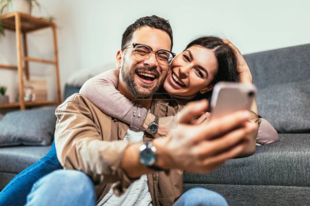 Photo for Beautiful young loving couple bonding to each other and making selfie while sitting on the couch together - Royalty Free Image
