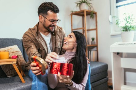 Téléchargez les photos : Man giving a surprise gift to woman at home. Party at home, birthday gift, anniversary, Valentines day and holiday - en image libre de droit