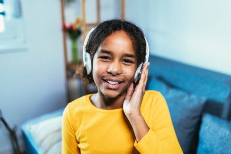 Foto de Chica afroamericana disfrutando del tiempo libre en casa mientras está sentado en la cama y escuchando música con auriculares - Imagen libre de derechos