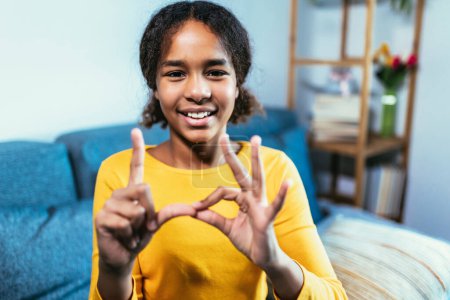 Foto de Hermosa sonriente chica sorda negra usando lenguaje de señas en casa - Imagen libre de derechos