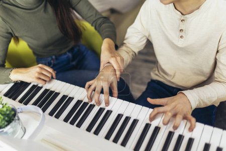 Photo for Brother and sister play electric piano at home and have fun. The sister helps her younger brother to play piano - Royalty Free Image