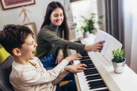 Foto de Brother and sister play electric piano at home and have fun. The sister helps her younger brother to play piano - Imagen libre de derechos