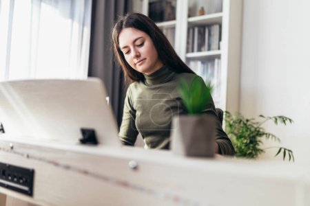 Foto de Happy girl is playing piano for her hobby relax time in home living room. Portrait Of Smiling Teenage Girl At Home Playing The Piano - Imagen libre de derechos