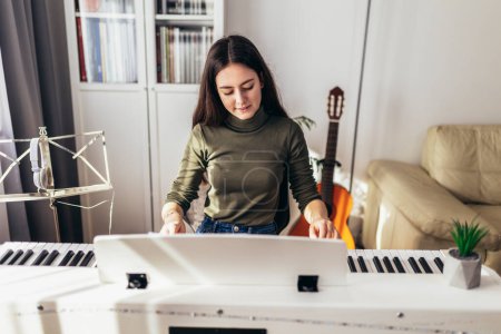 Téléchargez les photos : Happy girl is playing piano for her hobby relax time in home living room. Portrait Of Smiling Teenage Girl At Home Playing The Piano - en image libre de droit