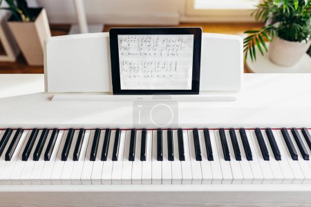 Téléchargez les photos : Vue sur une partie d'un piano avec tablette numérique comme partition musicale. - en image libre de droit