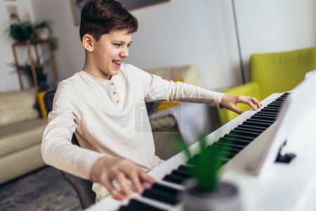 Foto de Little boy playing piano in living room. Child having fun with learning to play music instrument at home. - Imagen libre de derechos