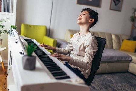 Photo for Little boy playing piano in living room. Child having fun with learning to play music instrument at home. - Royalty Free Image
