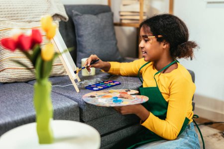 Foto de Preteen girl is using a paintbrush to bring creativity and color to life on a table, creating an indoor flower masterpiece. - Imagen libre de derechos