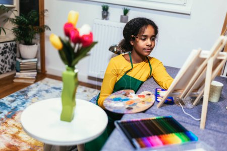 Téléchargez les photos : Preteen girl utilise un pinceau pour donner vie à la créativité et à la couleur sur une table, créant un chef-d'œuvre de fleurs d'intérieur. - en image libre de droit