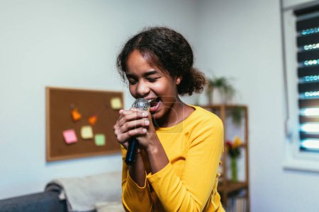 Téléchargez les photos : Cute preteen black girl  holding microphon singing karaoke at home, recording songs for contest. Children's lifestyle concept - en image libre de droit