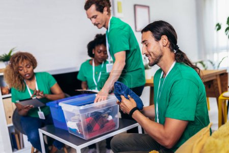 Foto de Voluntarios poniendo ropa en cajas de donaciones. Grupo de jóvenes voluntarios multiculturales en camisetas verdes que trabajan en el centro de caridad - Imagen libre de derechos