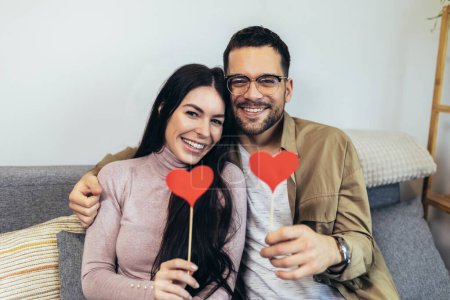 Foto de Happy smiling couple in love celebrating their relationship anniversary at home. Young couple holding a heart shape. - Imagen libre de derechos