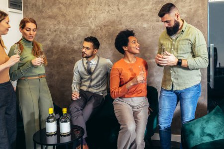Téléchargez les photos : Groupe de gens d'affaires assis ensemble dans un espace de coworking et célébrant avec une boisson alcoolisée. - en image libre de droit