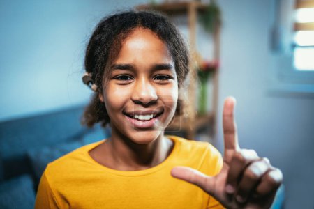 Téléchargez les photos : Belle fille sourde noire souriante utilisant le langage des signes à la maison - en image libre de droit