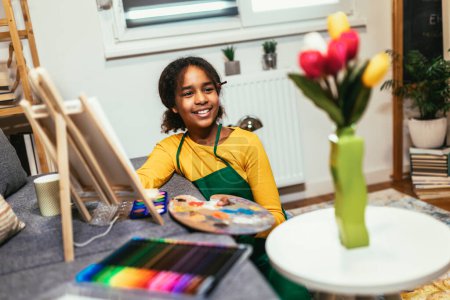 Foto de Chica preadolescente está utilizando un pincel para dar vida a la creatividad y el color en una mesa, la creación de una obra maestra de flores de interior. - Imagen libre de derechos