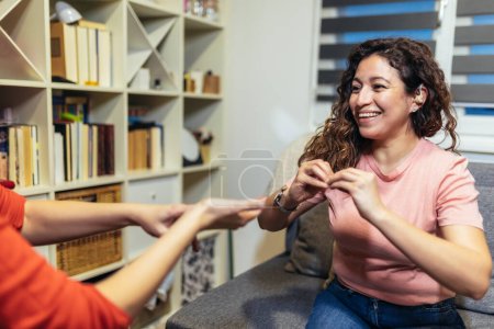 Téléchargez les photos : Femme sourde parlant la langue des signes avec son ami, assise sur le canapé. - en image libre de droit