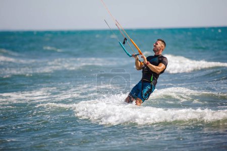 Foto de El kiter profesional hace el truco difícil. Un kiter macho cabalga sobre un hermoso fondo de olas y realiza todo tipo de maniobras. - Imagen libre de derechos